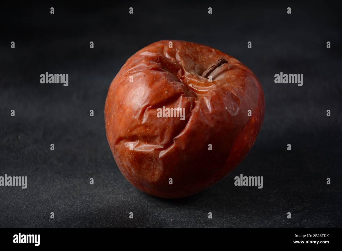 Rotten wrinkled skin apple on black background. Ugly food concept Stock Photo