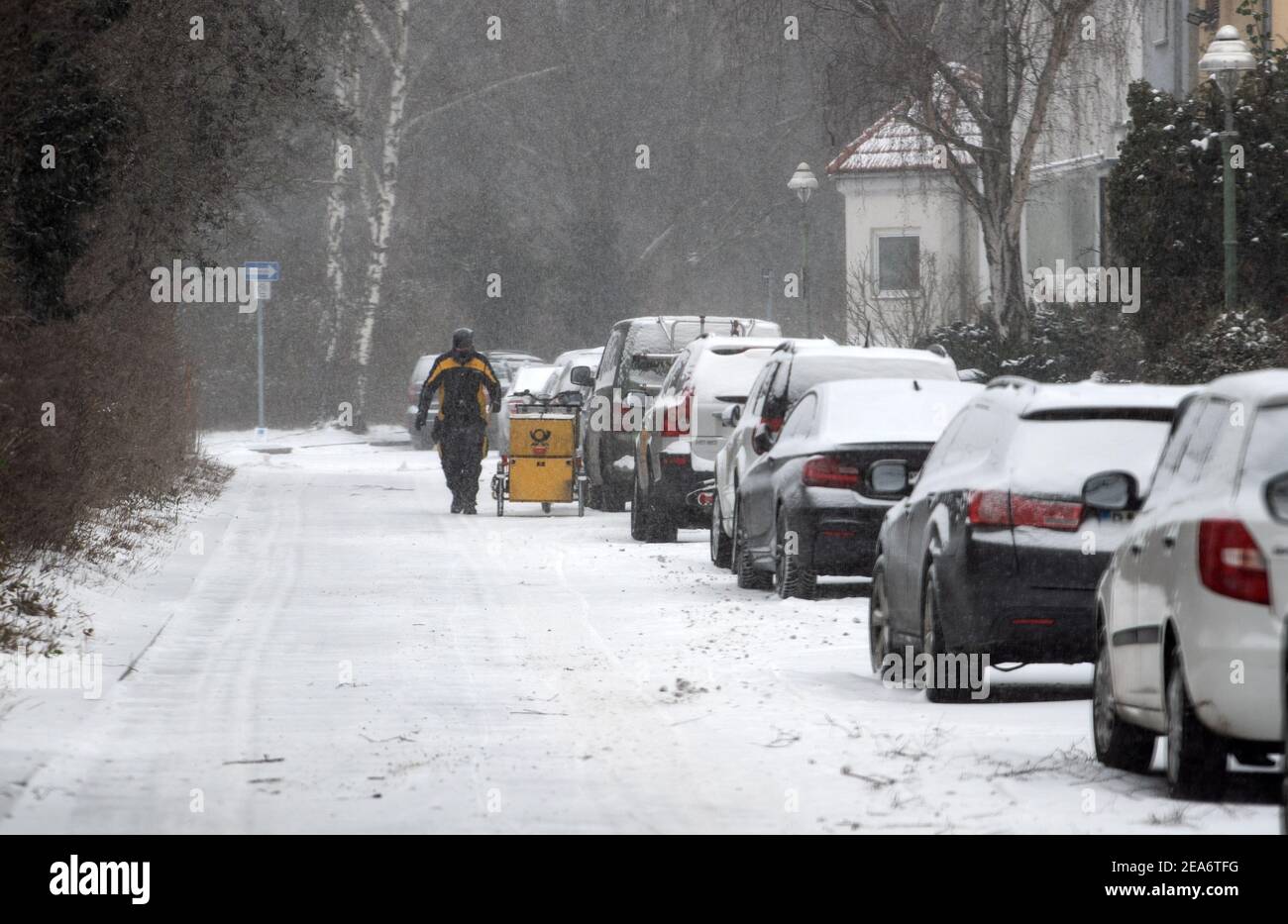 Berlin, Germany. 08th Feb, 2021. A postman walks to his cargo bike on a snowy street in