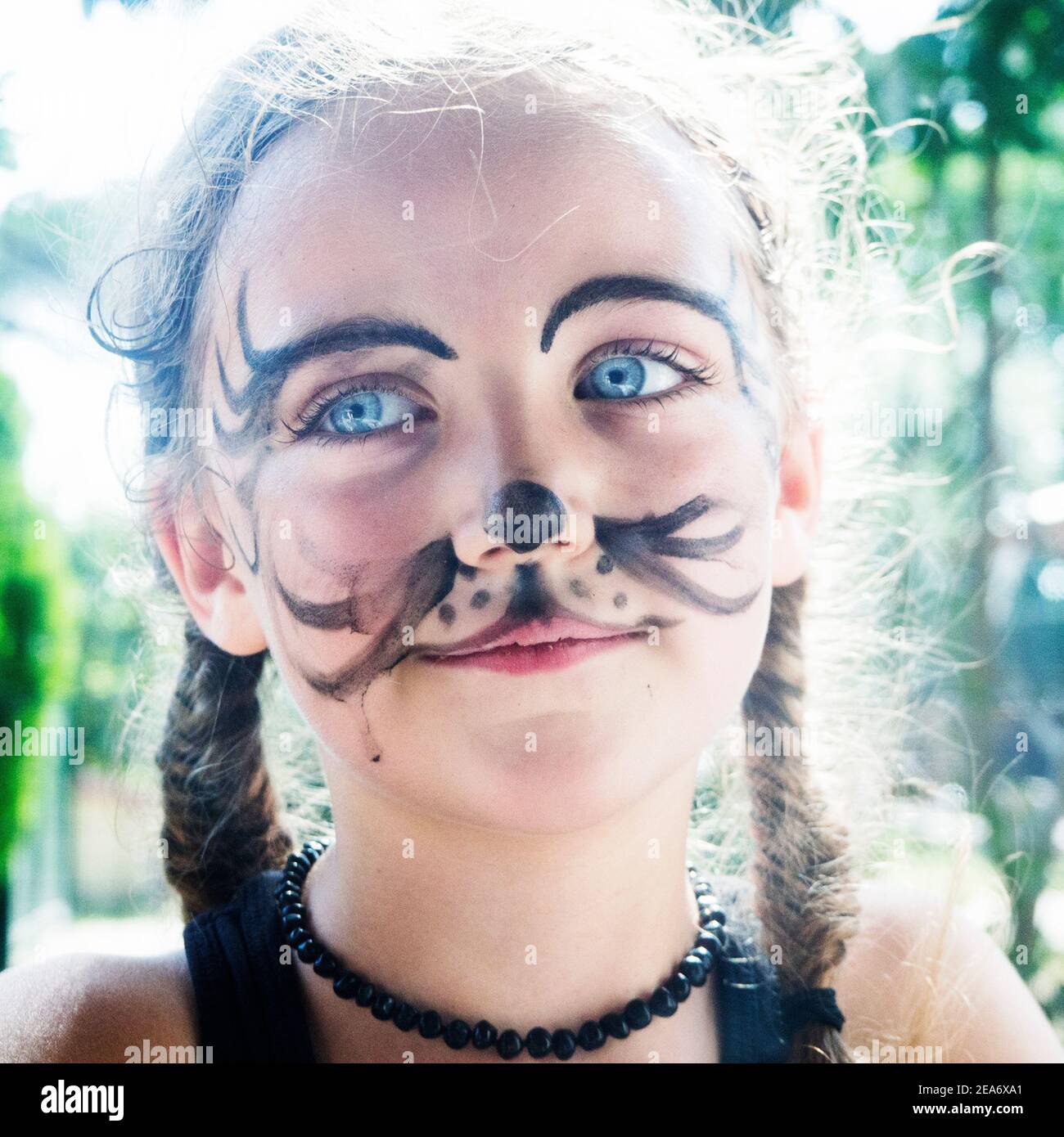 Close-up portrait of a smiling girl with tiger face paint standing in a garden, Italy Stock Photo