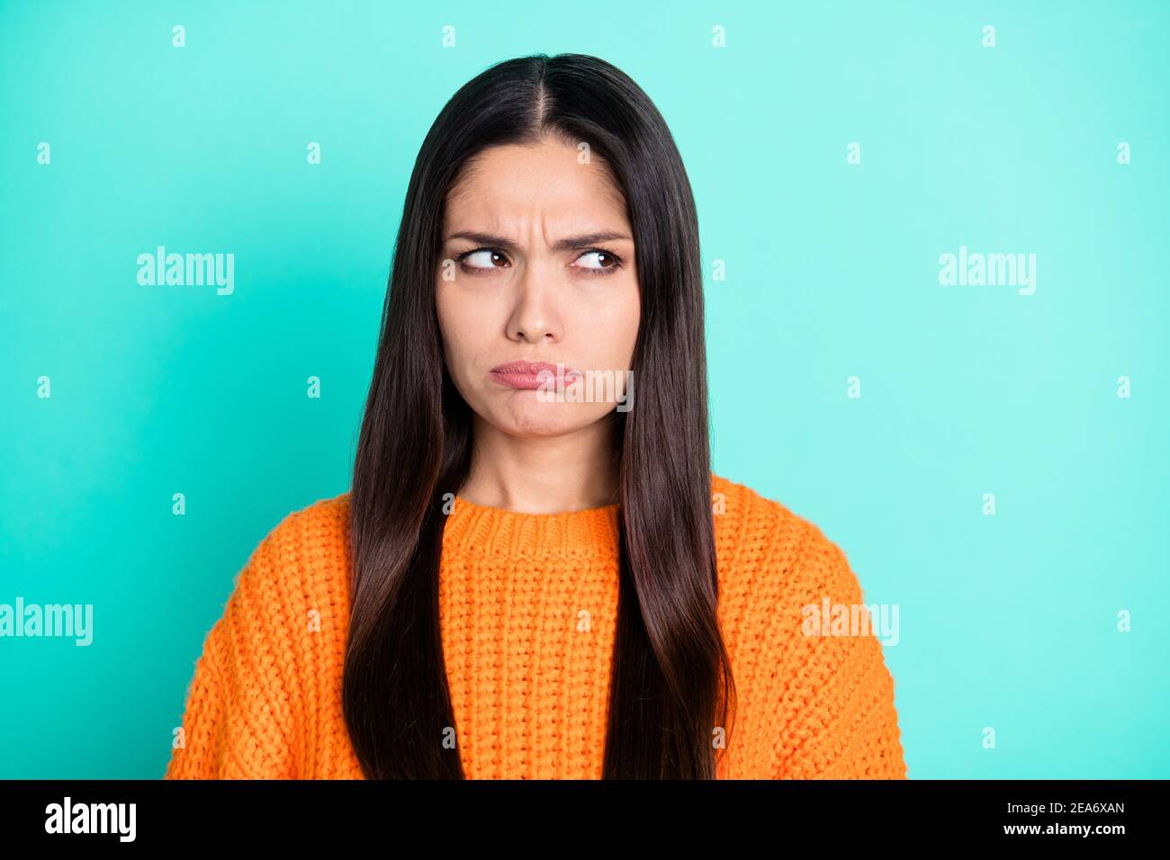 Photo of grumpy young woman look side empty space wear orange pullover isolated teal color background Stock Photo