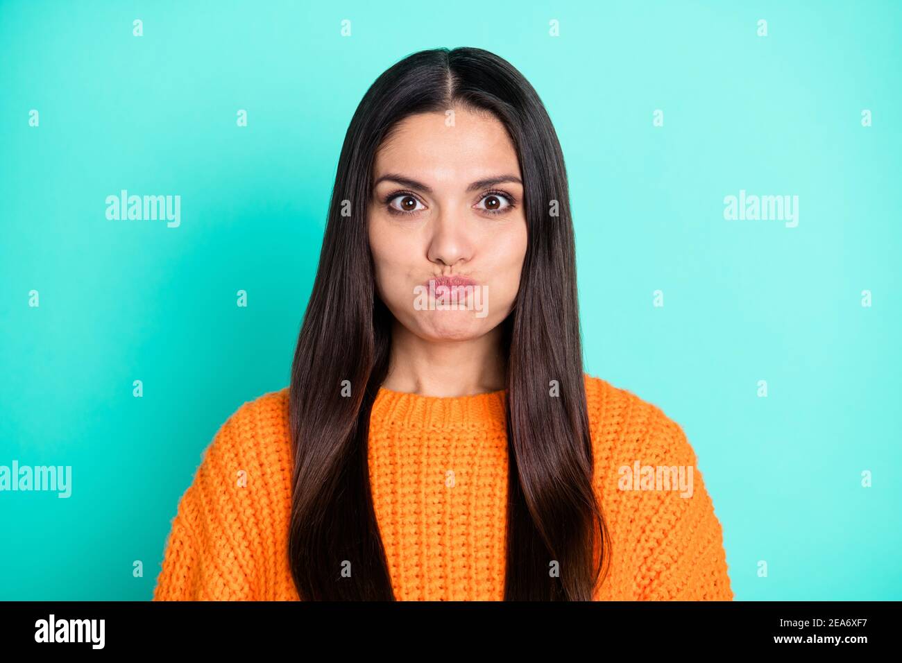 Photo of positive young lady inflate cheeks look camera have fun wear orange sweater isolated teal color background Stock Photo