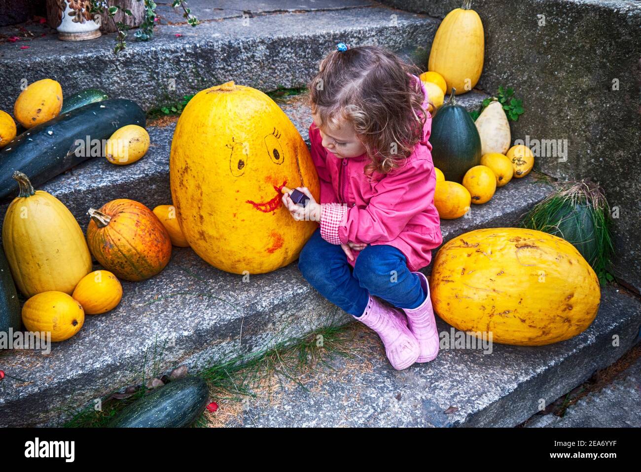 Girl sitting on a step drawing a smiley face on a Halloween pumpkin, Poland Stock Photo
