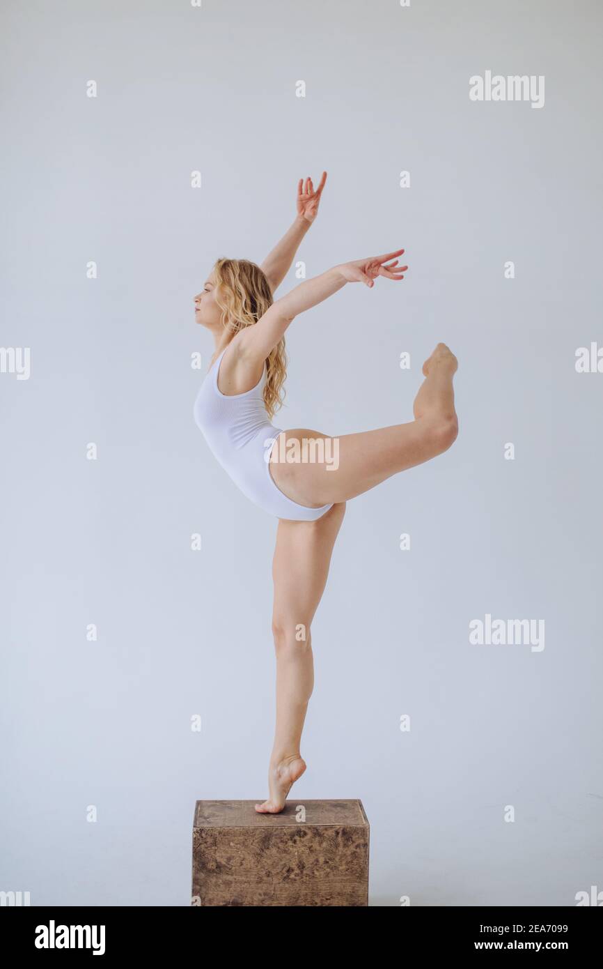 Female gymnast in a white leotard standing on one leg in a studio Stock Photo