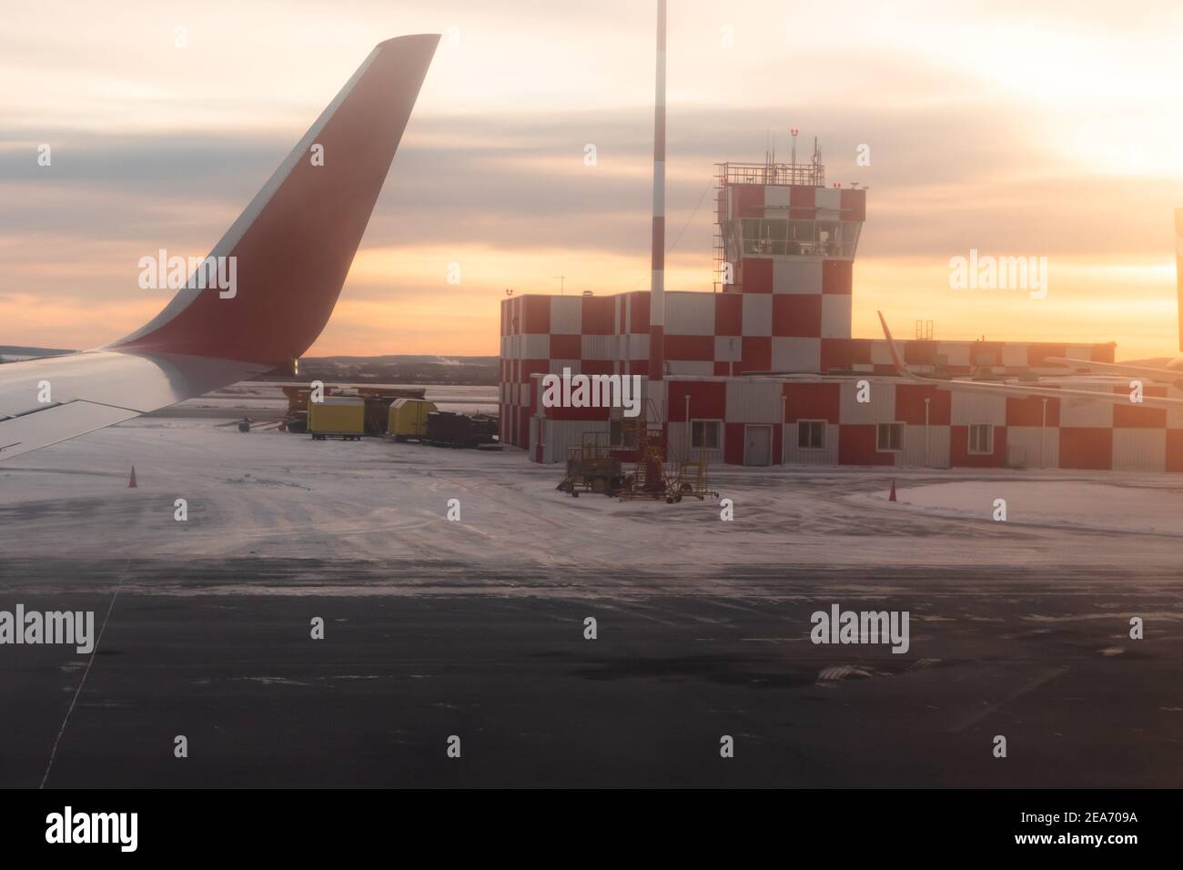 airport building at dawn on the runway with flashing beacon painted in red and white checkerboard squares. airplane window view Stock Photo