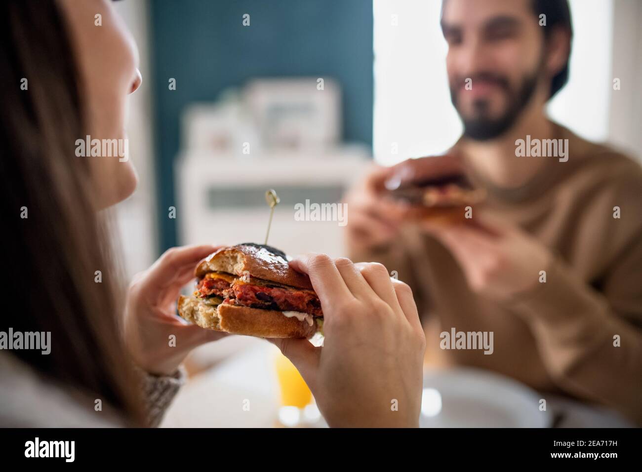 Unrecognizable young couple in love eating hamburgers indoors at home. Stock Photo