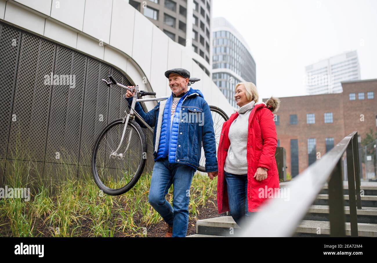 Happy senior couple with bicycle walking in city, holding hands. Stock Photo