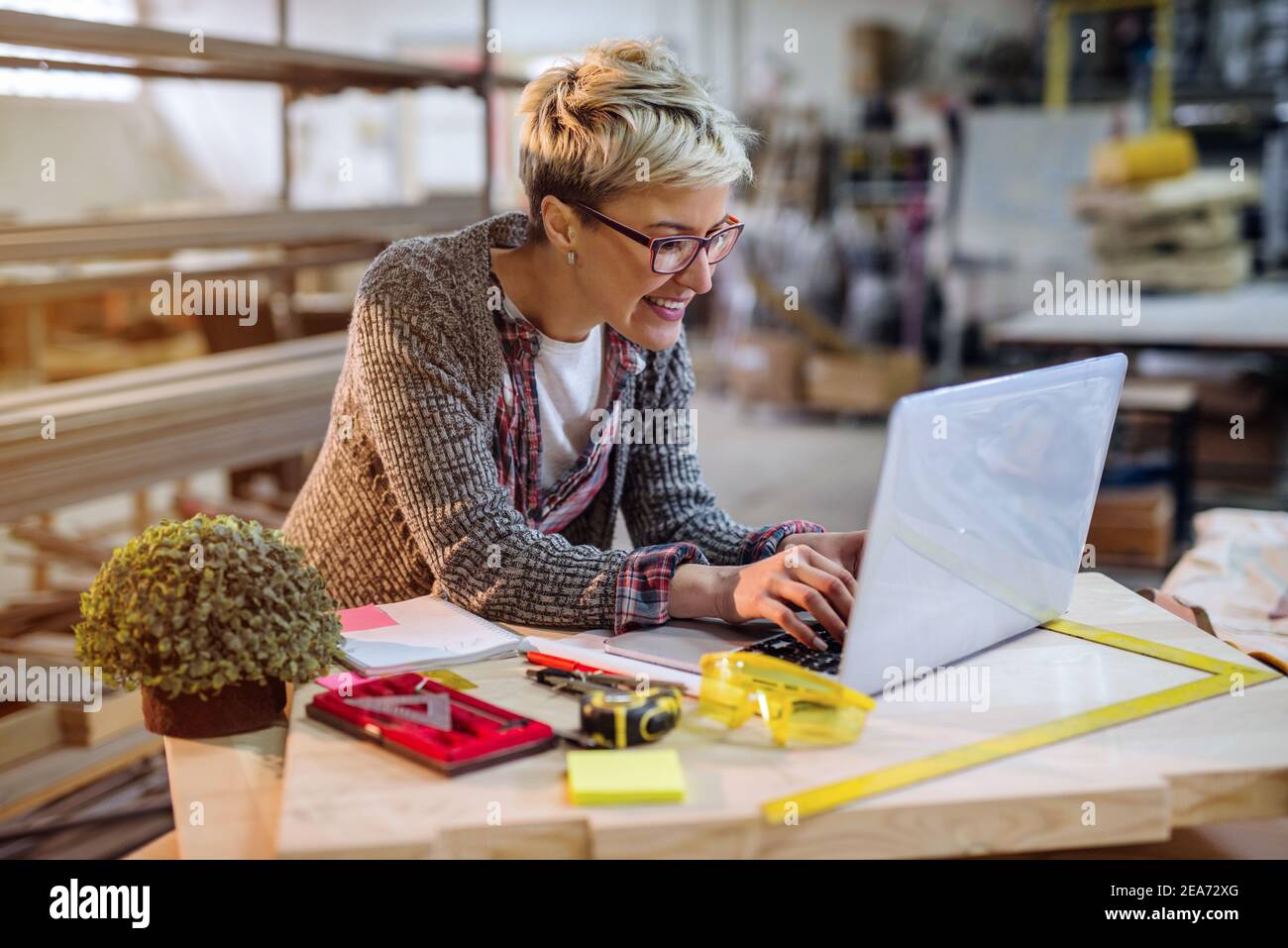 Female carpenter using laptop for calculations while standing in the workshop. Stock Photo