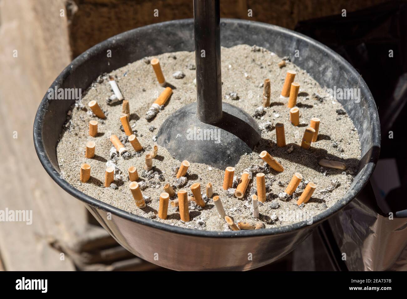 A round sand filled ashtray filled with extinguished cigarettes or dog ends Stock Photo