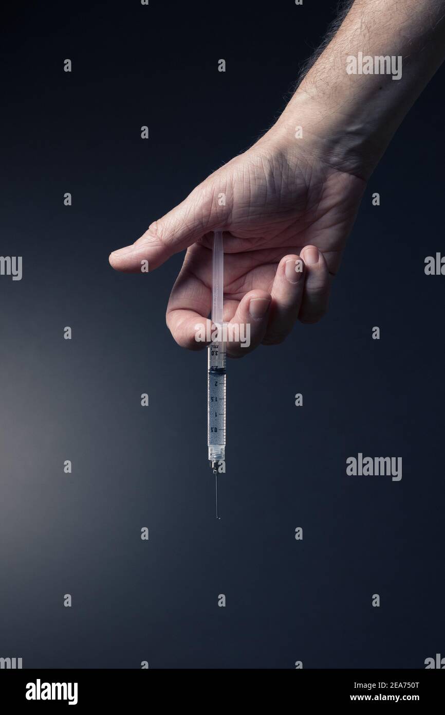 Colour image of man's hand holding syringe vertically downwards with