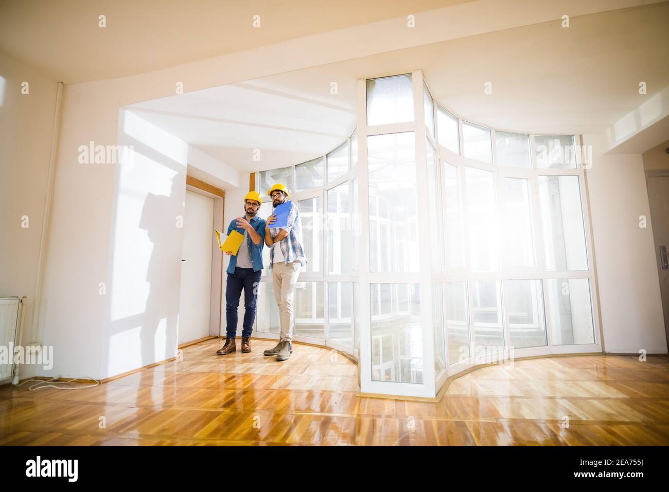 Two young male architects walking through an empty apartment a talking ...