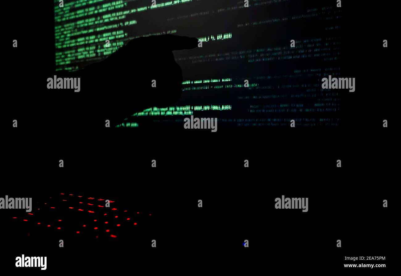 Hacker pointing to code on a computer monitor in a dark room.  Stock Photo