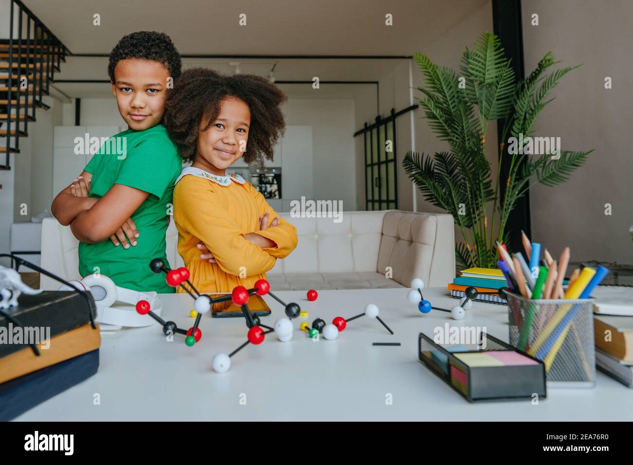 Sister and brother having fun standing in the living room near desk with school equipment. Back to school concept. Stock Photo