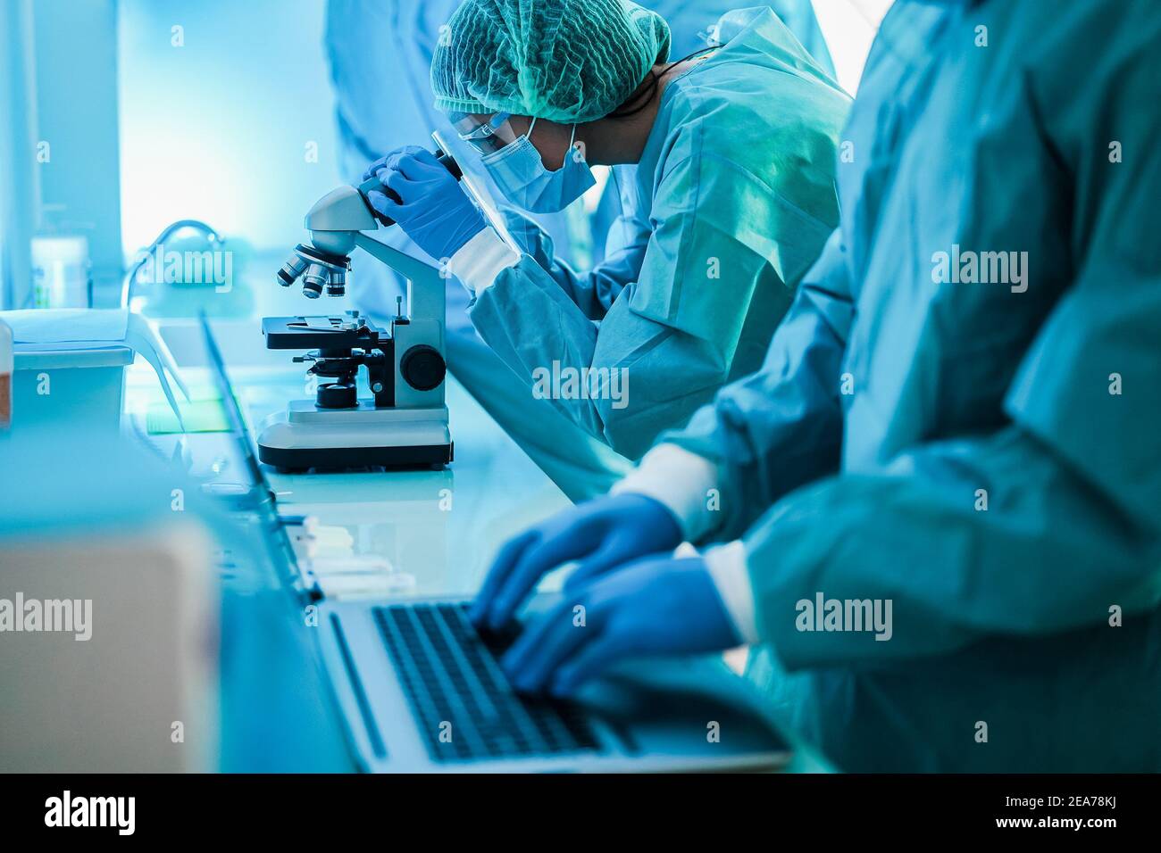 Medical scientist in hazmat suit working with microscope and laptop computer inside laboratory hospital - Focus on woman hand Stock Photo