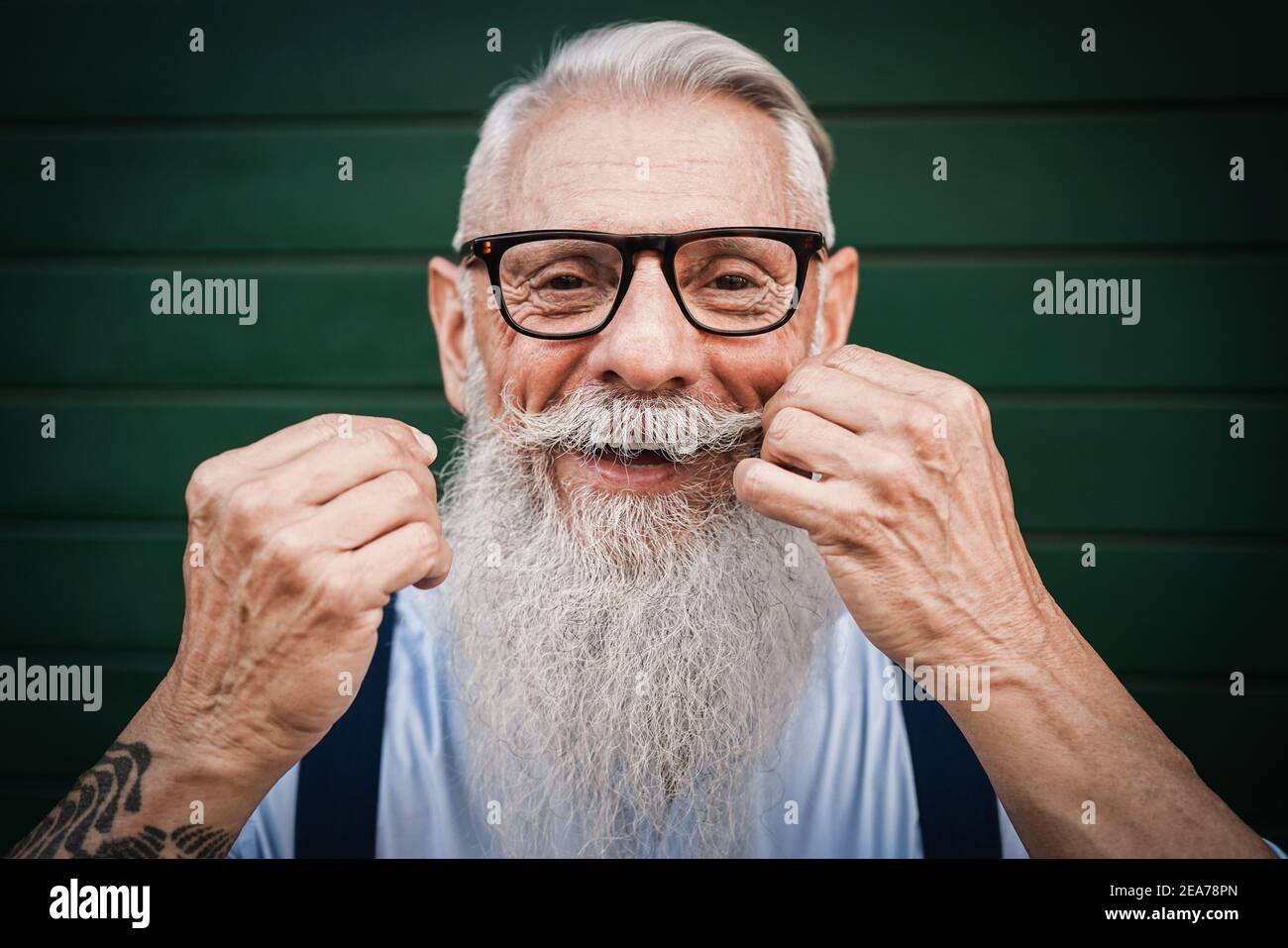 Portrait of happy hipster senior man with green background - Focus on mustache Stock Photo