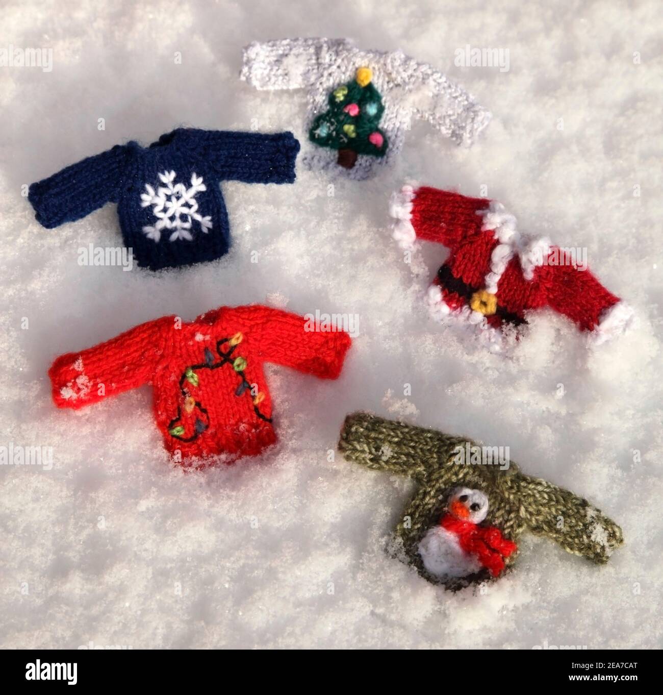 Selection of small knitted festive Christmas jumpers in the snow. Stock Photo