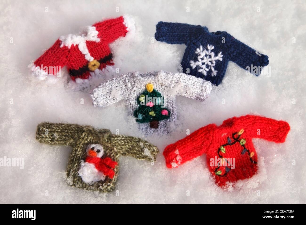 Selection of small knitted festive Christmas jumpers in the snow. Stock Photo