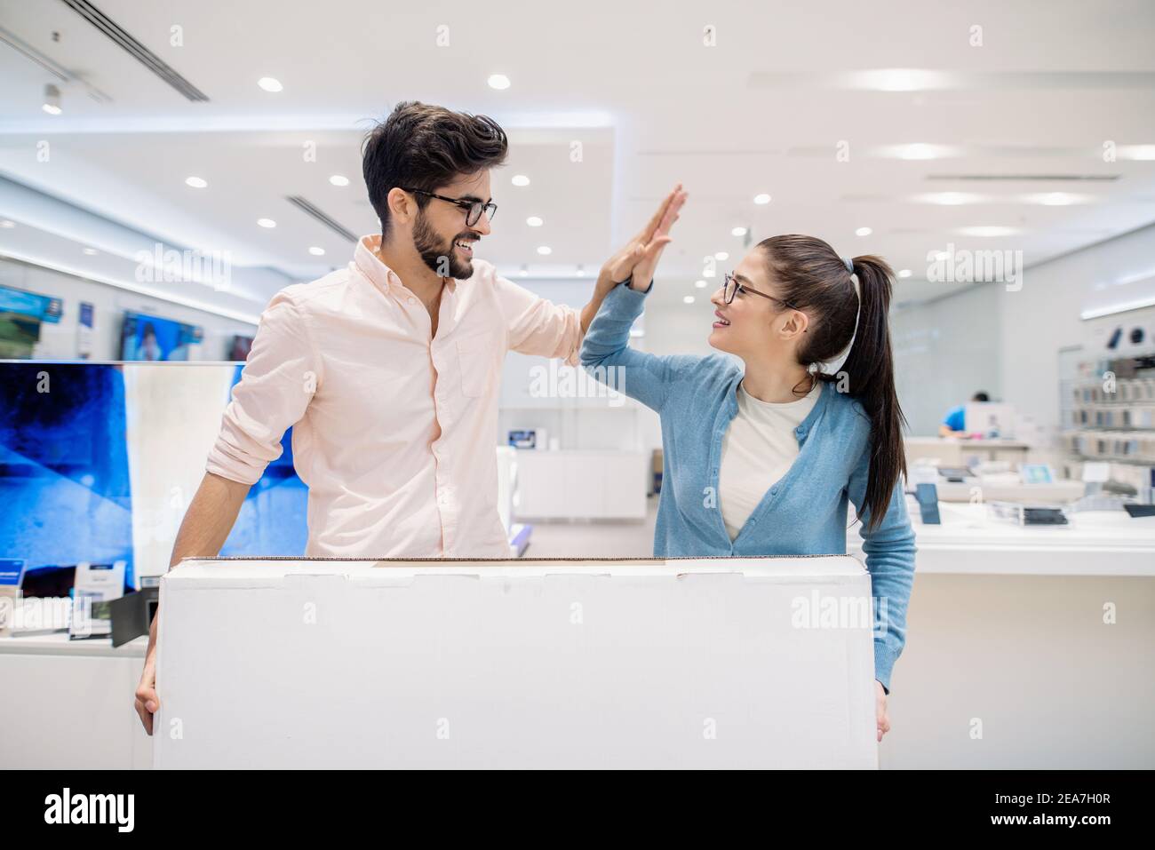 Happy couple buying plasma TV and giving high-five. Tech store interior. Stock Photo