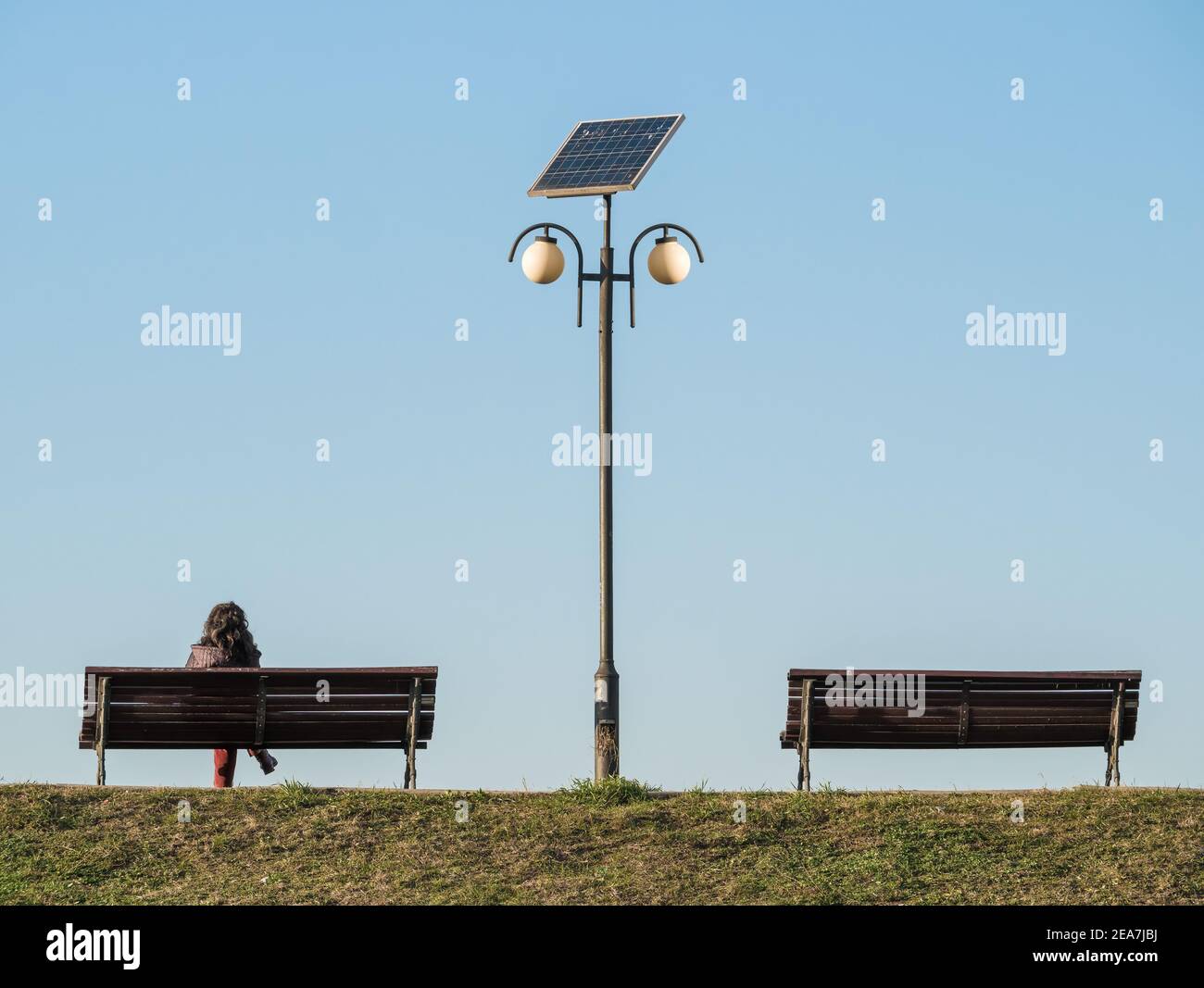 Lonely woman sitting on a bench next to a light pole. Two benches 