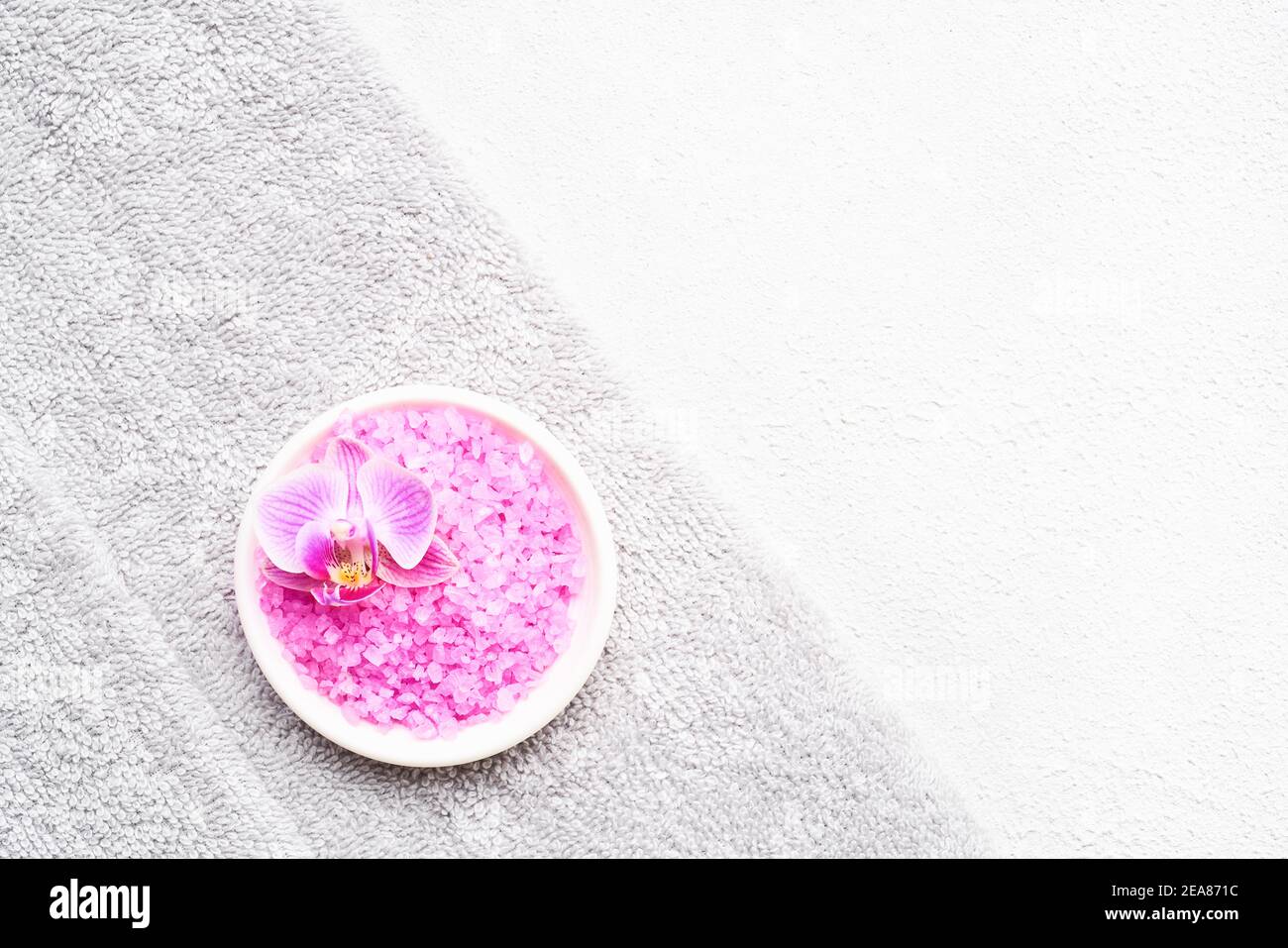 Rolled grey towels, pink bath salt, and orchid flower on a white concrete background. SPA, hygiene, wellness well-being, body care concept. Copy space, Stock Photo