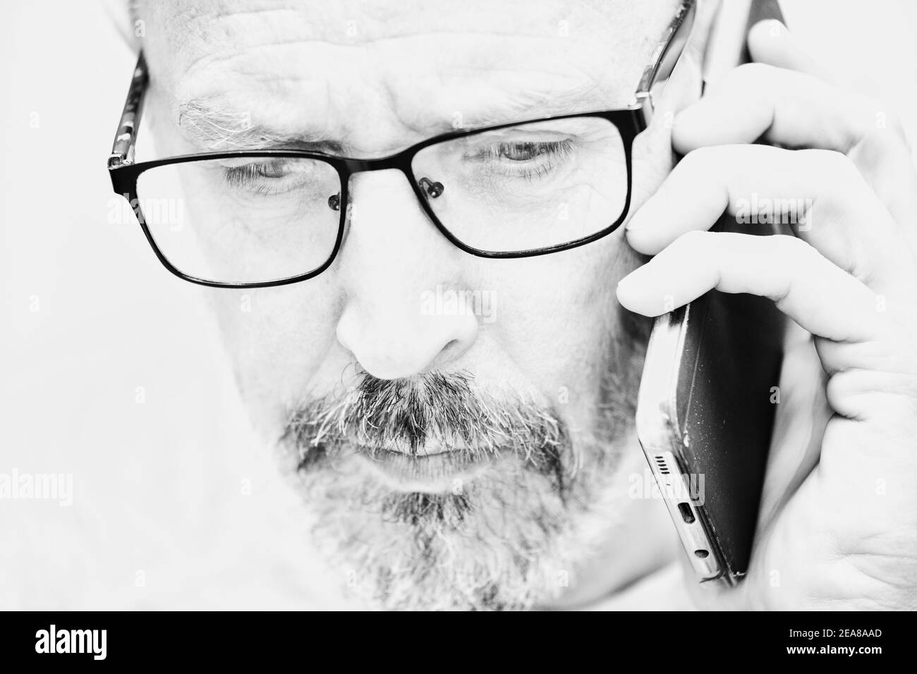 Black and white image of serious middle aged man with beard and glasses talking on smartphone. Concept of lifestyle, communication, technology Stock Photo