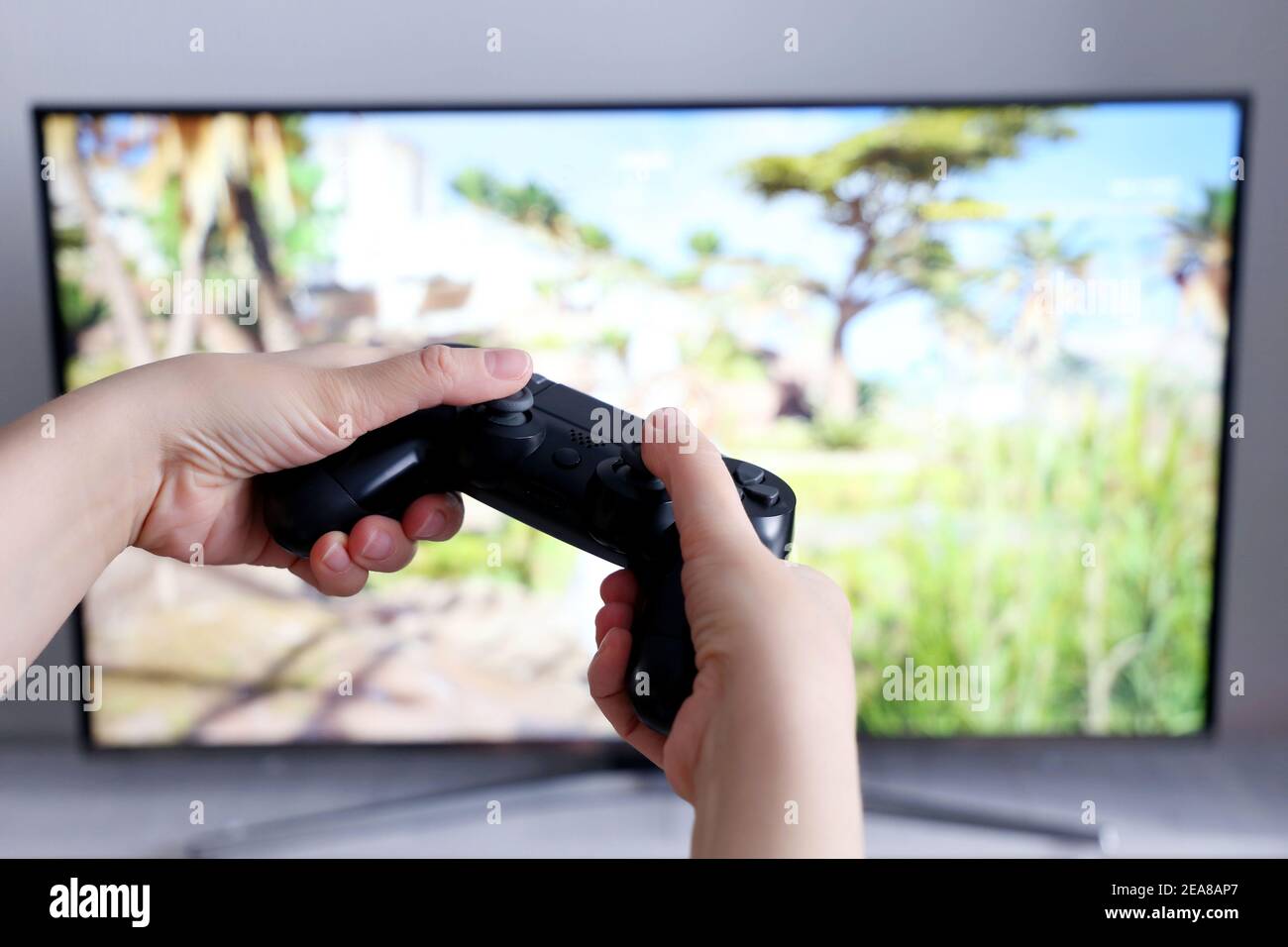 Gamepad in female hands closeup on TV screen background, gaming addiction concept. Girl gamer playing video games with joystick Stock Photo