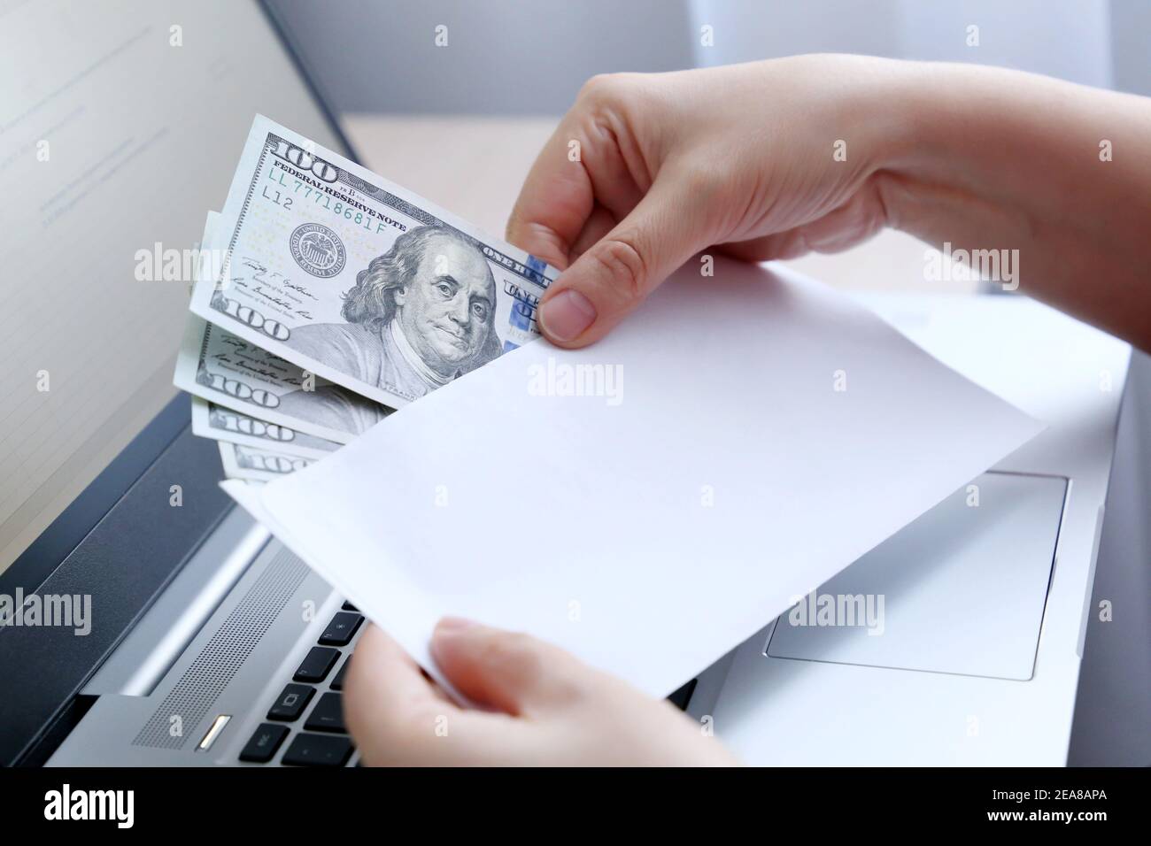 Envelope with US dollars in female hands. Woman pulls money out of an envelope on laptop background, wages, bonus or bribe concept Stock Photo