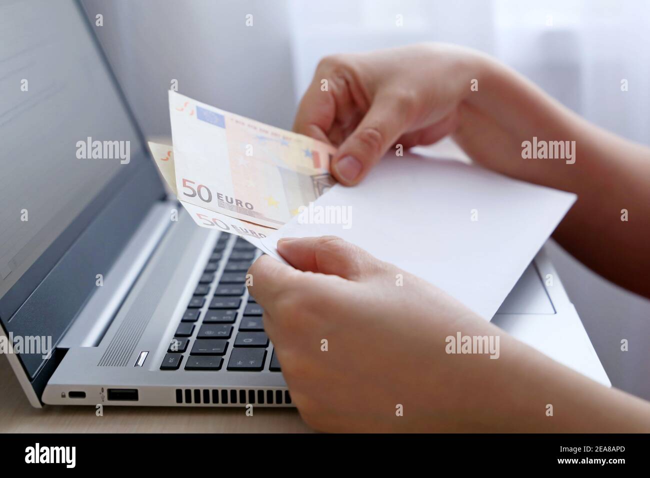 Envelope with euro banknotes in female hands. Woman pulls money out of an envelope on laptop background, wages, bonus or bribe concept Stock Photo