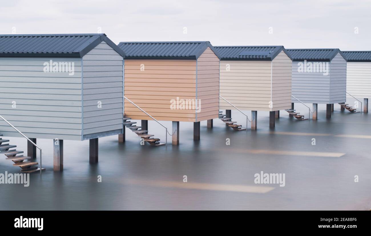 Line of beach huts up on stilts at high tide with smoothed water beneath Stock Photo