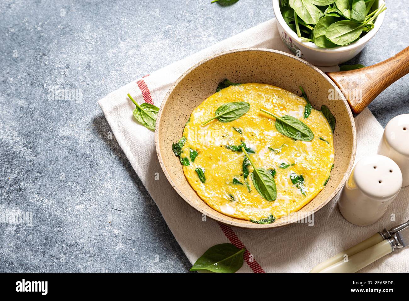 homemade egg omelet with spinach in a frying pan on a gray concrete background Stock Photo