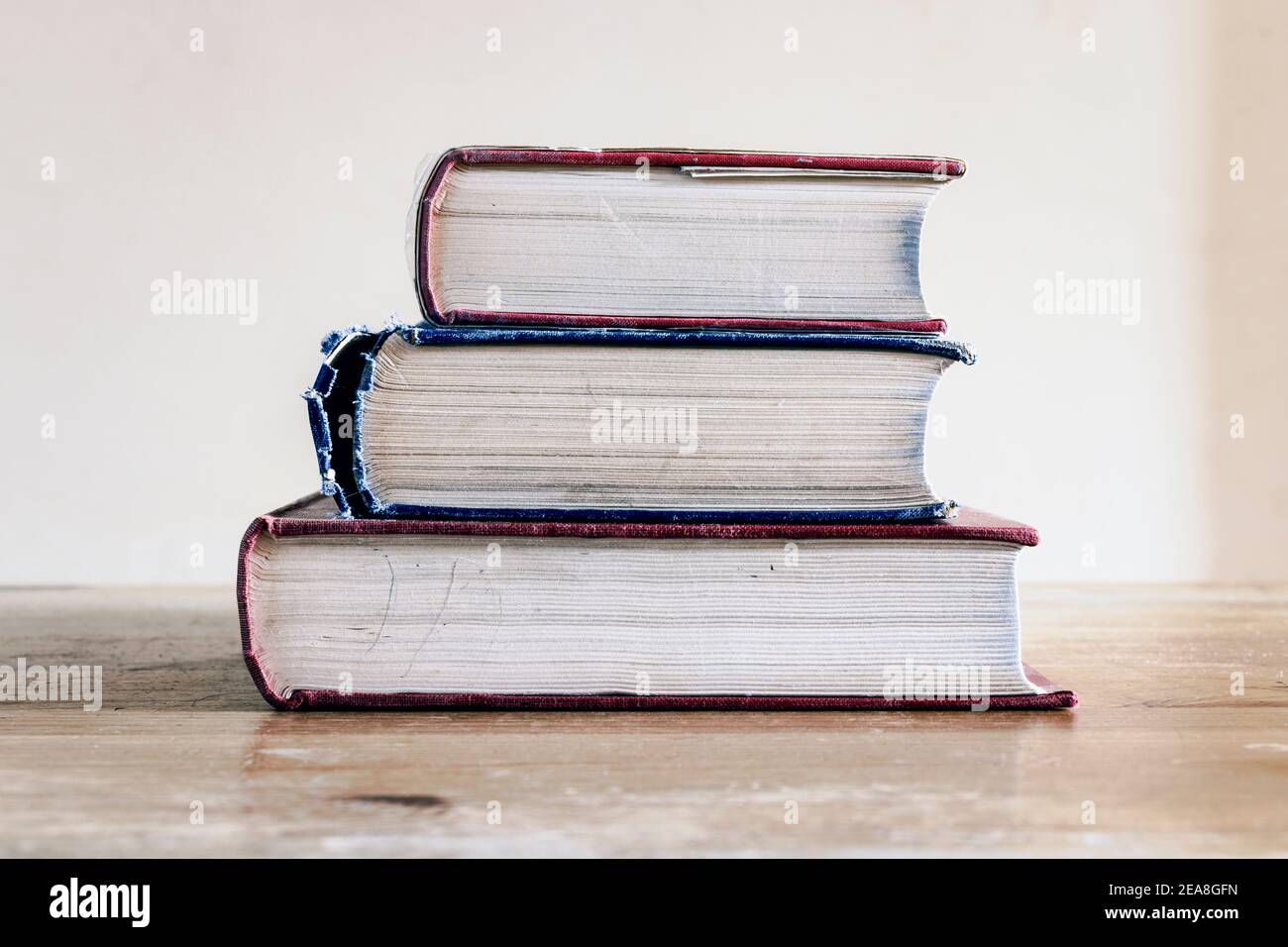 A stack of three old hardback reference books on an old wooden desk ...