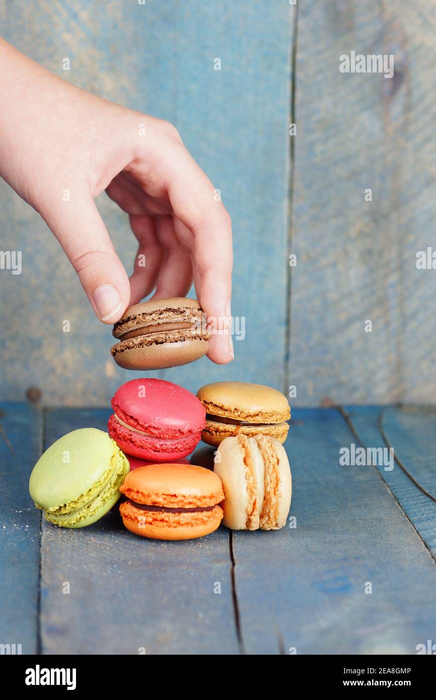 Vertical of hand picking macaroon, blue old wood background Stock Photo