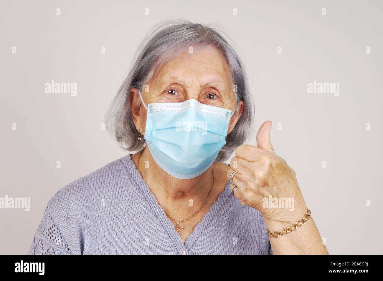 Happy masked senior woman with thumb up after receiving COVID vaccine Stock Photo