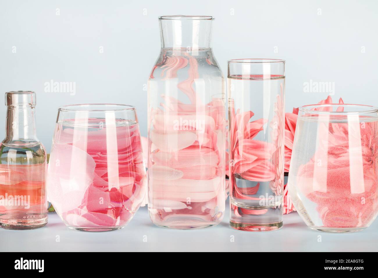 pink flowers distorted through water in glasses and bottle on blue background. Home decor, eco friendly, relax, gardening concept. copy space Stock Photo