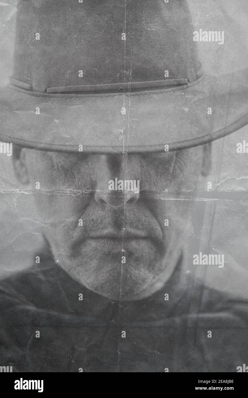 Black and white image of middle aged unshaven man with serious expression wearing cowboy hat covering his eyes. Moody, serious, intriguing close up Stock Photo
