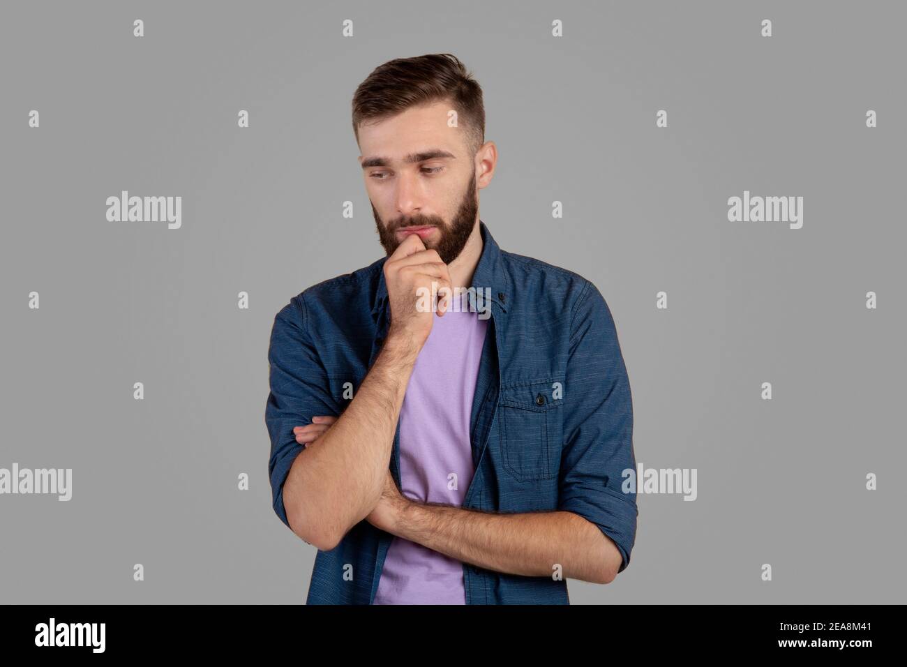 Dreamy young guy thinking over problem, touching his chin on grey studio background Stock Photo