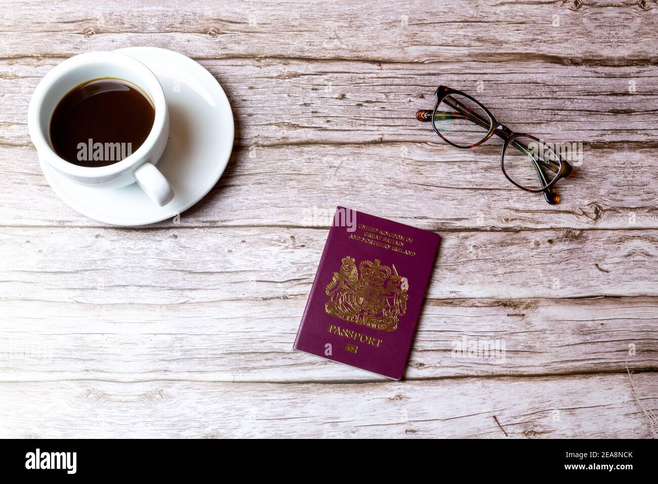 A Maroon British passport laid on a wooden table next to a coffee and a pair of glasses Stock Photo
