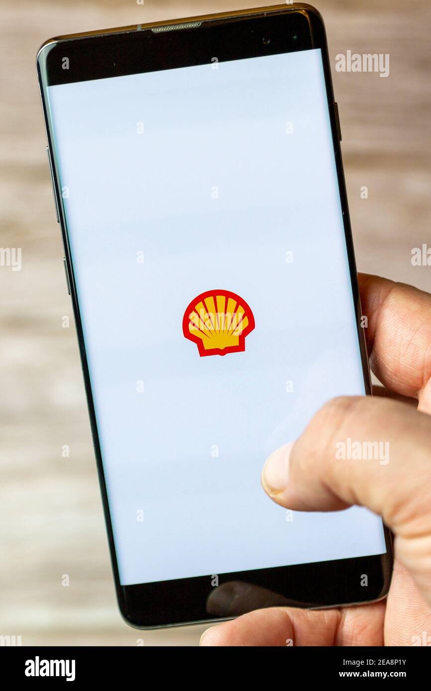 A mobile phone or cell phone being held in a hand with the Shell oil app open on screen Stock Photo