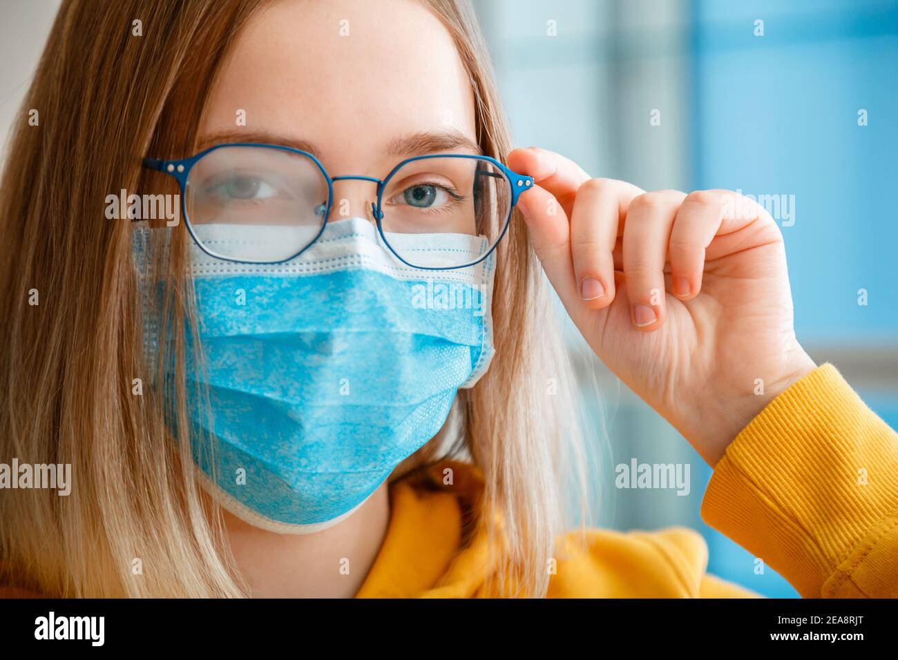 Foggy glasses wearing on young woman. close up portrait. Teenager girl in blue medical protective face mask and eyeglasses wipes blurred foggy misted Stock Photo