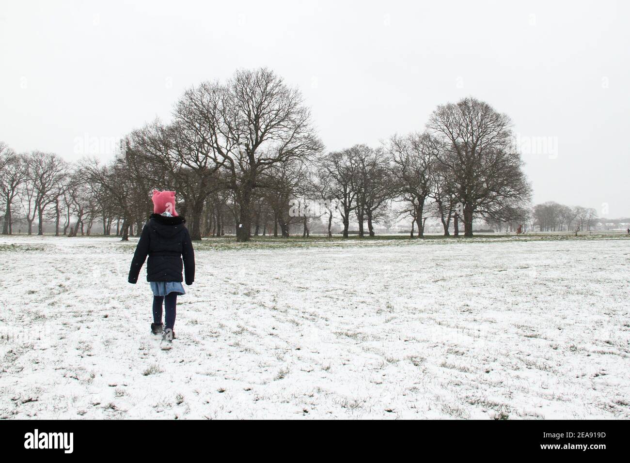 A young girl walks along a snow covered Wanstead Park. Heavy snow and ice has brought disruption to parts of the UK, with London receiving around 5cm of snow. Storm Darcy's strong easterly winds have plummeted temperatures in parts of the UK to below minus one. Stock Photo