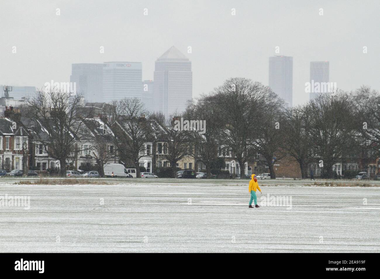 A man walks across a snow covered Wanstead Park with a backdrop of the Isle of Dogs skyscrapers. Heavy snow and ice has brought disruption to parts of the UK, with London receiving around 5cm of snow. Storm Darcy's strong easterly winds have plummeted temperatures in parts of the UK to below minus one. Stock Photo