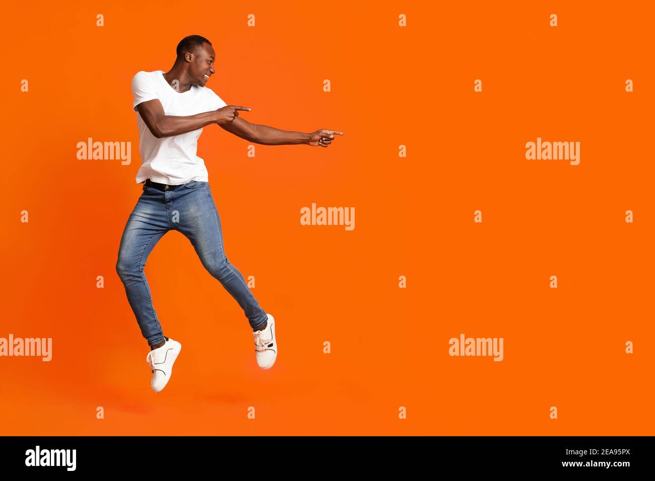 Millennial african american man pointing at copy space while jumping Stock Photo