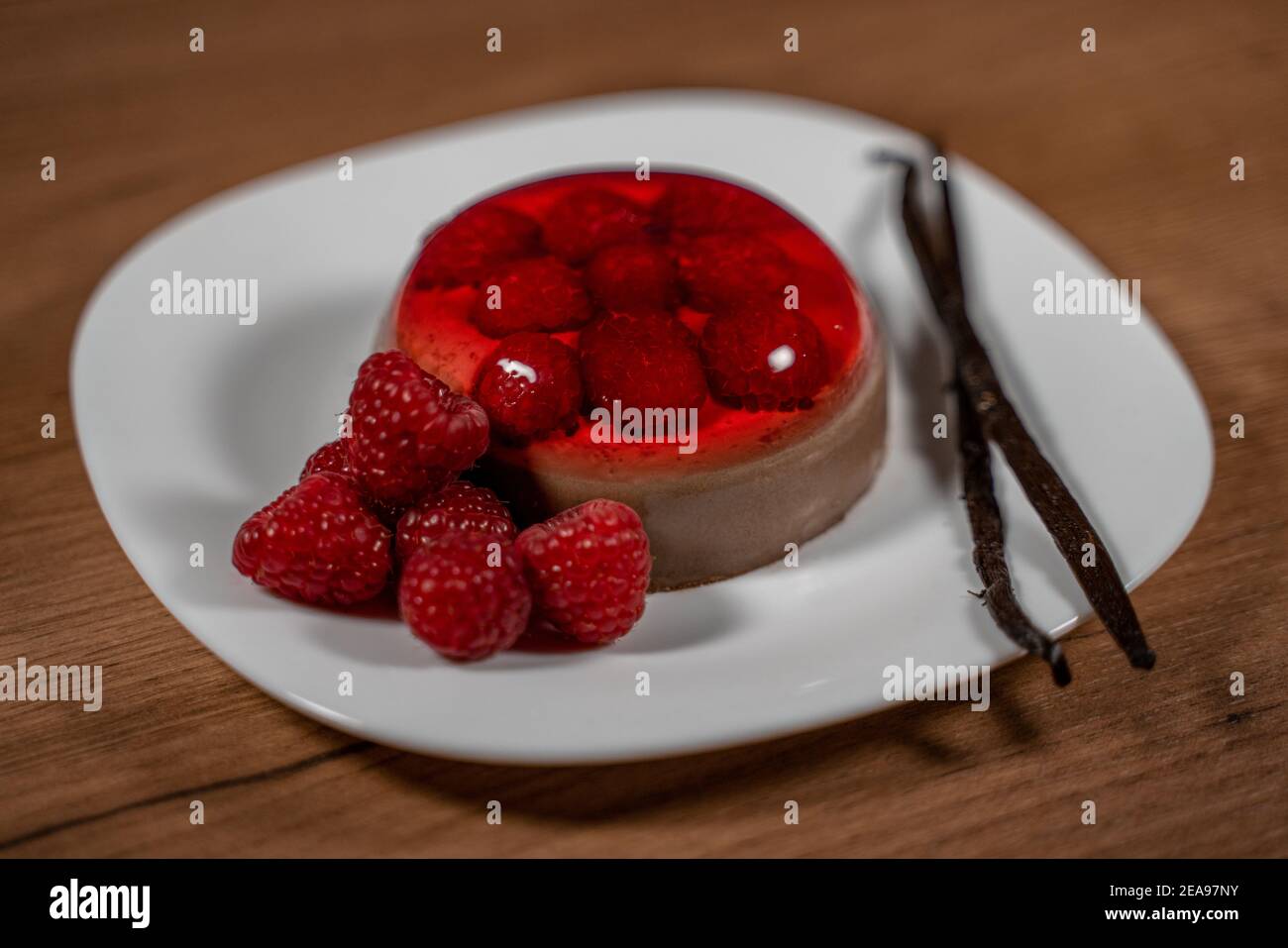 Chocolate pudding with raspberry jelly decorated with fresh raspberries and vanilla beans on white plate. Close-up image on wooden surface Stock Photo