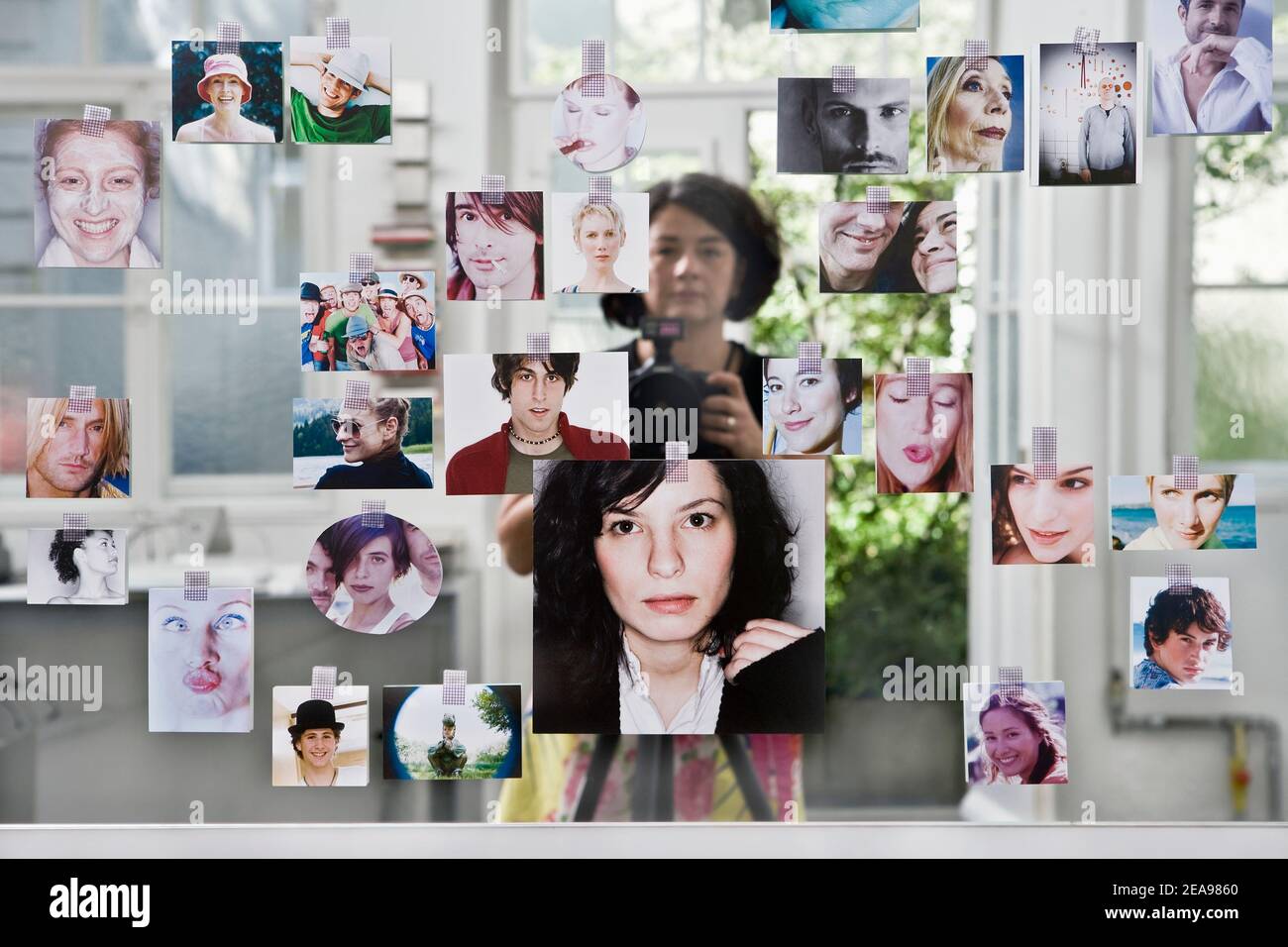 Woman photographed in a mirror, pasted with many portrait photos, in the background a door to the outside is reflected Stock Photo
