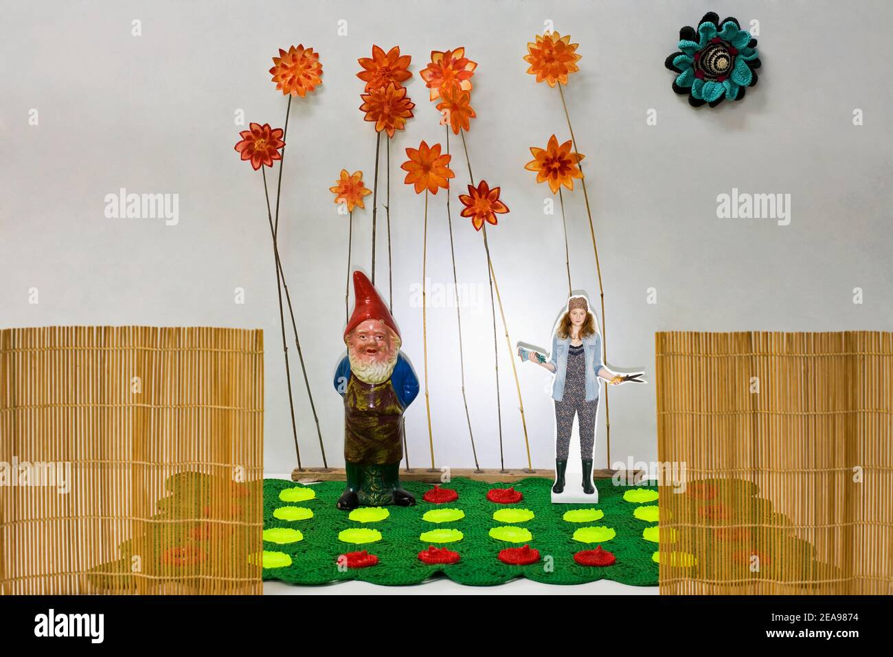 Still-life photo of cut-out woman, with garden gnome, in front of flower meadow, fence, with garden tools Stock Photo