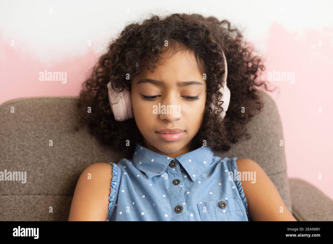 Upset African-American school-age girl looks down and feels offense. Difficult teen-age Stock Photo