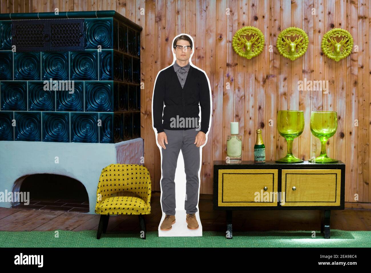 Photo collage, man next to armchair, in front of shelf and tiled stove, green carpet, glasses, yellow, deer antlers on the wall Stock Photo