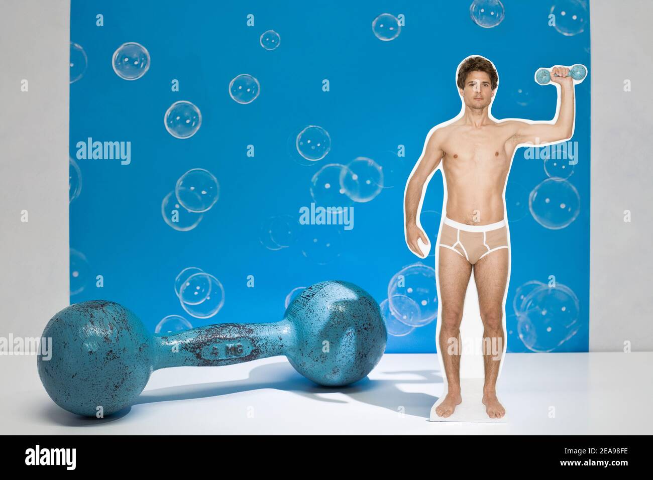 Cut-out photo of a man in underpants, holding a dumbbell in one hand, a real dumbbell lies next to him, background a photo with blue soap bubbles, background white Stock Photo