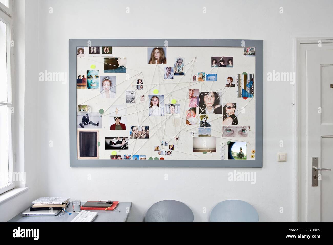 Pinboard with a gray frame, with portrait photos of different people, connected by a thread, cut in door, window, desk and chairs, white background Stock Photo