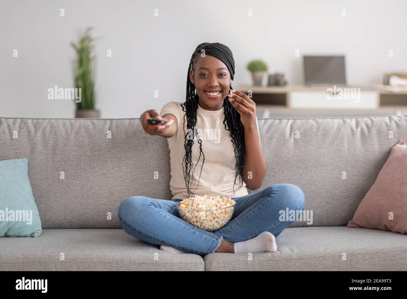 Happy black woman sitting on couch with TV remote Stock Photo