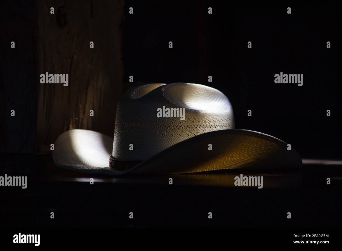 A straw cowboy hat sits on top of a bar.  It's lit from natural light through some overhead windows. Stock Photo